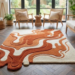 Pode incluir: Um tapete retangular grande com um design abstrato em tons de laranja e creme. O tapete apresenta um padrão fluido e marmoreado, adicionando um toque moderno à sala de estar. O tapete está colocado sobre um chão de madeira escura. Cerca de 200 cm x 300 cm.