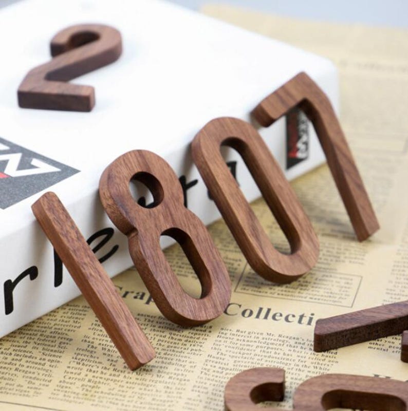May include: Wooden numbers in a warm brown hue, arranged on a white surface and vintage newspaper. The numbers include 2, 1, 8, 0, and 7. The numbers are made of wood and have a natural finish.