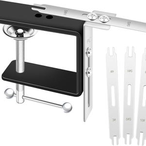 May include: A black and silver clamp-style tool with a screw mechanism and adjustable arm. Three silver metal pieces with markings are positioned next to the clamp. The tool is designed for holding objects.