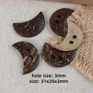 May include: Four crescent moon-shaped buttons with two holes each. Three buttons are dark brown with a textured grain, and one is a lighter beige colour. The text on the image states: hole size: 3mm, size: 31x20x3mm. These buttons have a smooth finish.