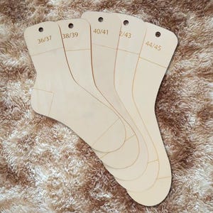 Könnte beinhalten: Ein Set aus fünf hellen Sockenbrettern aus Holz, die fächerförmig angeordnet sind. Jedes flache, fußförmige Brett hat ein Loch zum Aufhängen an der Oberseite und ist mit den Größen 36/37, 38/39, 40/41, 42/43 und 44/45 graviert.