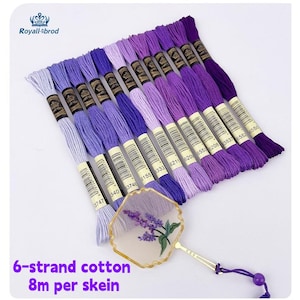 Può includere: Una collezione di matassine di filo da ricamo viola in varie tonalità, disposte diagonalmente. L'immagine include un ventaglio decorativo con un design di lavanda e il testo "6-strand cotton 8m per skein."