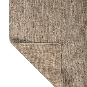 May include: A neutral-toned area rug with a woven texture. The rug's corner is folded back, revealing the underside. The color is a mix of beige and brown, suitable for various interior styles.