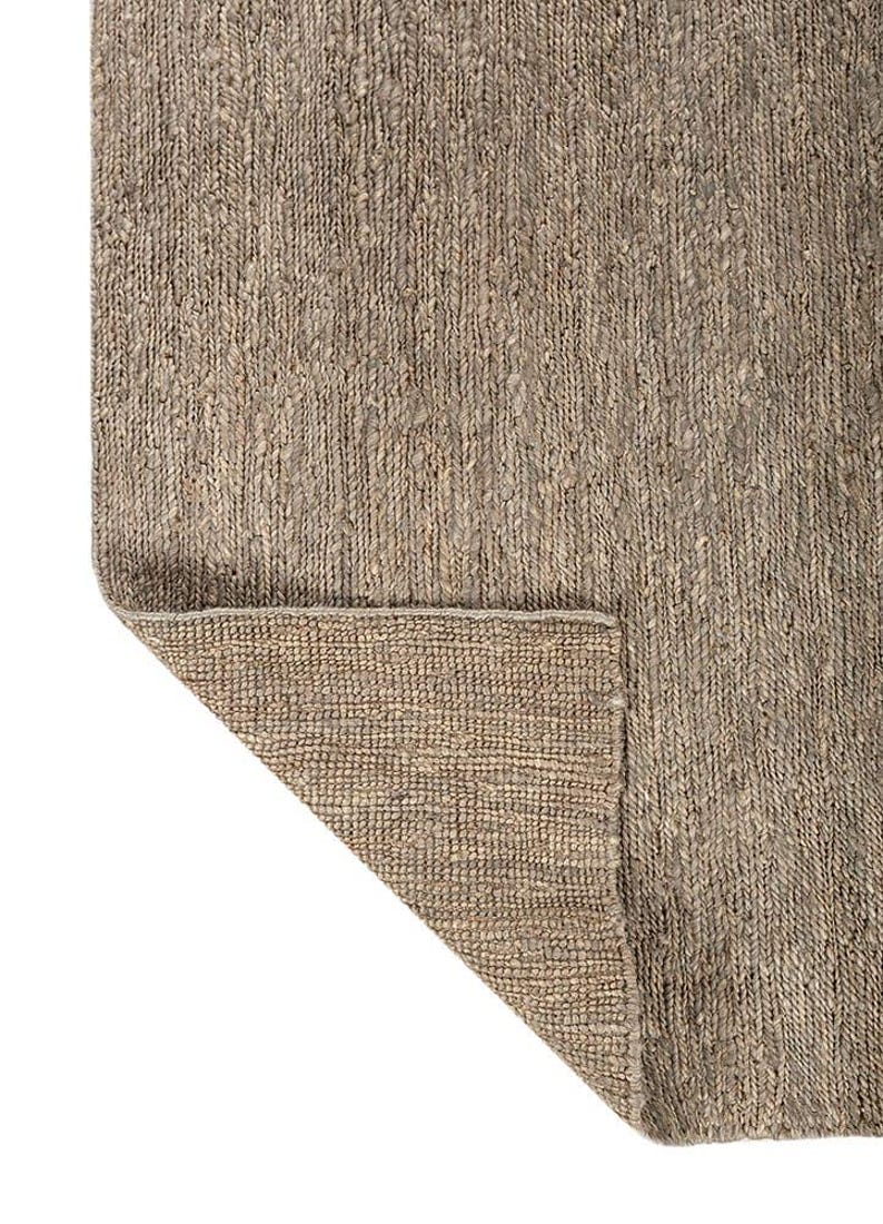 May include: A neutral-toned area rug with a woven texture. The rug's corner is folded back, revealing the underside. The color is a mix of beige and brown, suitable for various interior styles.