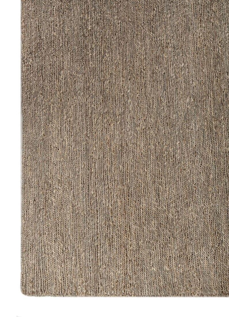May include: A close-up of a rectangular, woven rug in shades of brown and tan. The rug has a textured surface with vertical lines, creating a natural, rustic appearance. The rug's corner is visible against a white background.