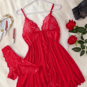 A vibrant red lace lingerie set laid flat against a soft, textured background features a sheer nightdress with a deep v-neckline, delicate floral lace cups, thin shoulder straps, and a front bow accent alongside matching lace panties.