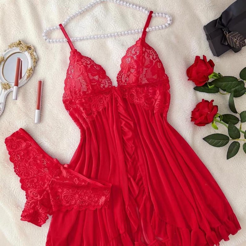 A vibrant red lace lingerie set laid flat against a soft, textured background features a sheer nightdress with a deep v-neckline, delicate floral lace cups, thin shoulder straps, and a front bow accent alongside matching lace panties.