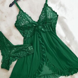 A vibrant green lace lingerie set laid flat against a soft, textured background features a sheer nightdress with a deep v-neckline, delicate floral lace cups, thin shoulder straps, and a front bow accent alongside matching lace panties.