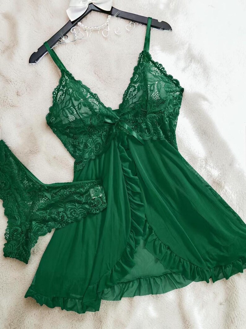 A vibrant green lace lingerie set laid flat against a soft, textured background features a sheer nightdress with a deep v-neckline, delicate floral lace cups, thin shoulder straps, and a front bow accent alongside matching lace panties.