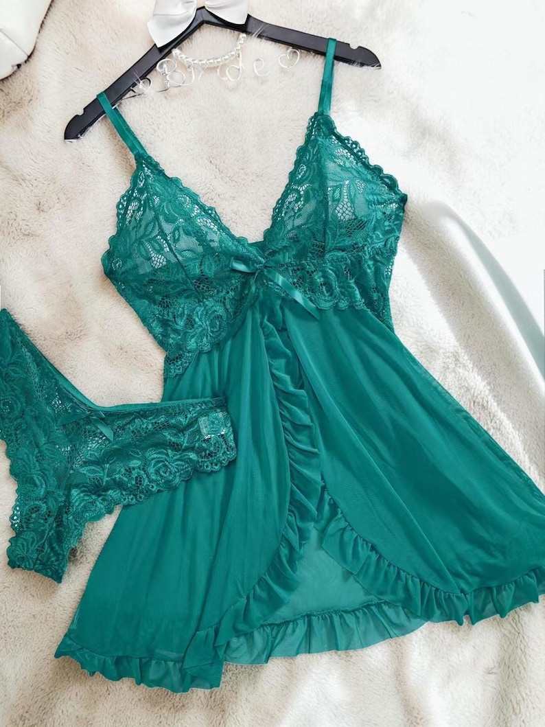 A vibrant peacock green lace lingerie set laid flat against a soft, textured background features a sheer nightdress with a deep v-neckline, delicate floral lace cups, thin shoulder straps, and a front bow accent alongside matching lace panties.