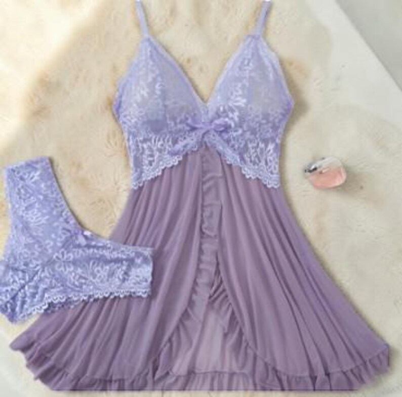 A vibrant purple lace lingerie set laid flat against a soft, textured background features a sheer nightdress with a deep v-neckline, delicate floral lace cups, thin shoulder straps, and a front bow accent alongside matching lace panties.