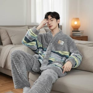 以下が含まれることがあります： グレーのぬいぐるみパジャマセット。トップスはボタンフロントで、胸と袖に青、緑、黄色のストライプ模様があります。パンツは無地のグレーです。セットは柔らかくふわふわした素材で作られています。