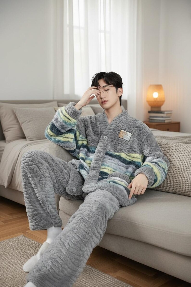 以下が含まれることがあります： グレーのぬいぐるみパジャマセット。トップスはボタンフロントで、胸と袖に青、緑、黄色のストライプ模様があります。パンツは無地のグレーです。セットは柔らかくふわふわした素材で作られています。