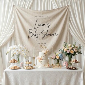 May include: A baby shower table setting with a two-tiered cake, flowers, and desserts. A banner reads "Welcome to Liam's Baby Shower." The table is set with various treats, candles, and floral arrangements, creating a celebratory atmosphere.