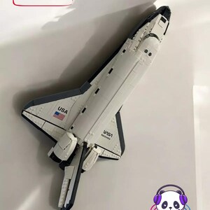 Könnte beinhalten: Ein weiß-schwarzes Space-Shuttle-Modell mit dem Schriftzug USA und NASA Discovery auf dem Rumpf. Ein rot umrandeter Kasten enthält den Text ORIGINALPRODUKT NICHT ENTHALTEN! - KOMPATIBLES ZUBEHÖR! sowie ein Panda-Logo mit dem Schriftzug WONDERPRINT.EU.