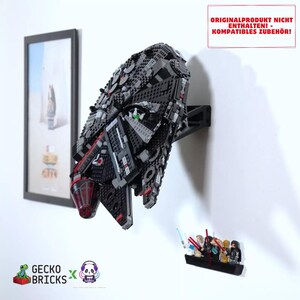 Könnte beinhalten: Eine schwarze Kunststoff-Wandhalterung mit einem großen, detaillierten schwarzen und grauen Raumschiffmodell. Der Text ORIGINALPRODUKT NICHT ENTHALTEN! - KOMPATIBLES ZUBEHÖR! steht in einem roten Kasten. Ein kleines schwarzes Regal zeigt mehrere Minifiguren.