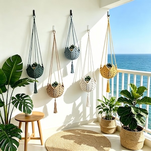 Puede incluir: Una colección de colgadores de plantas de macramé en varios colores, incluyendo verde, beige, azul, blanco y amarillo, cada uno con una pequeña planta en maceta. Los colgadores están suspendidos de ganchos en una pared blanca, con un balcón con vistas al mar en el fondo.