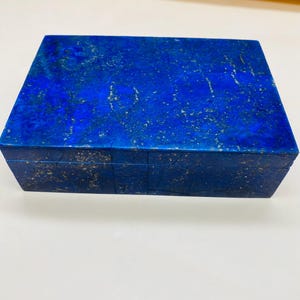 Puede incluir: Una caja rectangular azul oscuro con una superficie texturizada. La caja tiene tapa y parece estar hecha de un material similar a la piedra. El color es un azul rico y saturado con motas más claras.