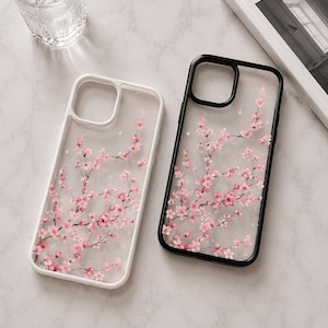 Peut inclure: Deux coques de smartphone, l'une avec un cadre blanc et l'autre avec un cadre noir, présentant toutes deux un dos transparent orné d'un motif délicat de branches de cerisiers en fleurs roses. Les coques sont rectangulaires avec des coins arrondis.