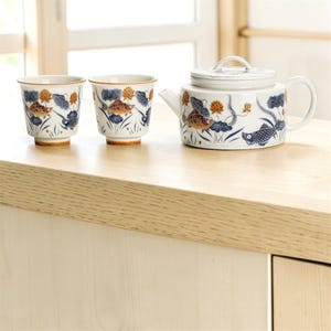 May include: A white ceramic mug with a black handle and the text "But First, Coffee" in a handwritten style. The mug is on a white surface. The mug is approximately 4 inches tall.
