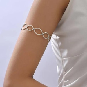 May include: A silver-toned arm cuff featuring a continuous, repeating infinity or figure-eight pattern. The metal band is smooth and polished, designed to wrap around the upper arm, creating a series of interconnected oval shapes in a row.