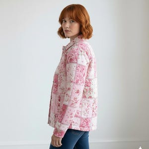 K&ouml;nnte beinhalten: Rosa gesteppte Jacke mit floralem Patchwork-Design. Die Jacke hat eine Knopfleiste vorne und einen Kragen. Das Blumenmuster umfasst Rosa- und Wei&szlig;t&ouml;ne. Die Person tr&auml;gt eine blaue Jeans.
