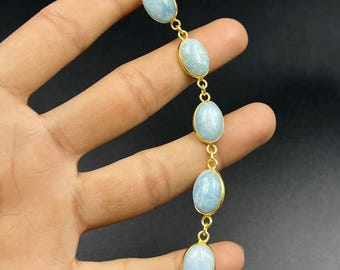 May include: A gold bracelet with oval, pale blue gemstones. The gemstones are set in gold bezels and linked with small gold connectors. The bracelet is shown against a dark background.