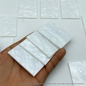 May include: A collection of rectangular white acrylic pieces featuring a marbled, pearlescent finish. Several of these smooth, flat, rectangular components are stacked together, displaying a consistent cloudy white pattern throughout the material.