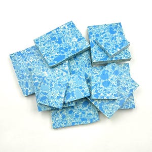 May include: A collection of square and rectangular tiles featuring a speckled pattern of various shades of blue and white. The tiles are arranged in a scattered, overlapping pile, displaying a consistent mottled texture across all surfaces.