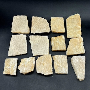May include: A collection of thirteen flat, rectangular pieces of light beige and tan stone with visible crystalline textures and irregular, rough-cut edges. The stones are arranged in a grid-like pattern, displaying varied shades of cream and gold.