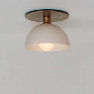 May include: A modern ceiling light fixture with a cream-colored, dome-shaped shade and a brass-colored base. The light bulb is visible and emits a warm glow. The fixture is designed for indoor use.