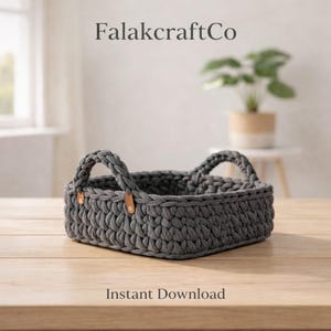 Puede incluir: Una cesta rectangular gris de ganchillo con dos asas. La cesta tiene un aspecto texturizado y está sobre una superficie de madera. El texto "FalakcraftCo" está en la parte superior y "Instant Download" en la inferior.