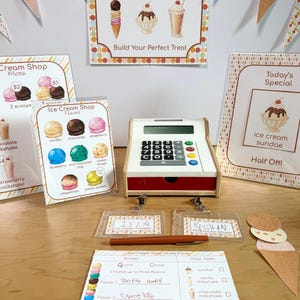 May include: A toy cash register, ice cream shop signs, name badges for Isla and Keghan, and an order form. The signs feature illustrations of ice cream cones, sundaes, and milkshakes with text including Ice Cream Shop, Flavors, and Today's Special.