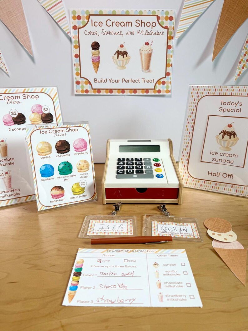 May include: A toy cash register, ice cream shop signs, name badges for Isla and Keghan, and an order form. The signs feature illustrations of ice cream cones, sundaes, and milkshakes with text including Ice Cream Shop, Flavors, and Today's Special.