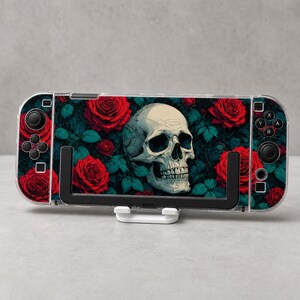 Puede incluir: Una consola de juegos portátil con una pegatina que muestra un cráneo humano central rodeado de rosas rojas vibrantes y follaje verde azulado oscuro. El dispositivo incluye botones de control negros, joysticks y una funda protectora.