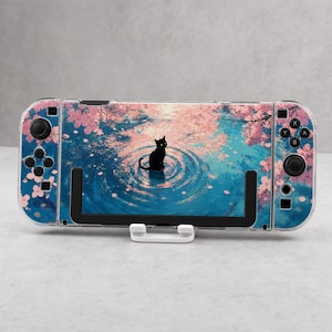 May include: A handheld gaming console featuring a protective skin with a graphic of a black cat sitting in blue water surrounded by pink cherry blossom trees. The console includes black joysticks, directional buttons, and action buttons on the sides.