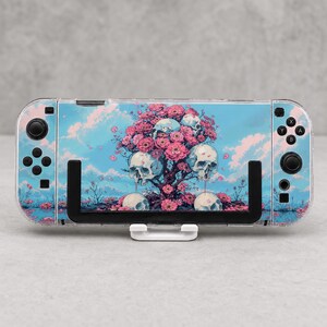 Può includere: Una console di gioco portatile dotata di una pellicola protettiva con un cielo azzurro, alberi di ciliegio in fiore rosa e diversi teschi umani integrati tra i rami. Il dispositivo include joystick e pulsanti neri.