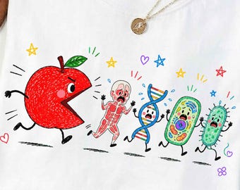 May include: A white t-shirt featuring a graphic print of a large red apple chasing a human anatomical figure, a DNA strand, a plant cell, and a bacterium. The design includes colorful hand-drawn stars and hearts scattered around the characters.