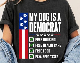 May include: A charcoal gray short-sleeve t-shirt featuring the text MY DOG IS A DEMOCRAT with a vertical American flag design, paw prints, and a checklist including Free Housing, Free Health Care, Free Food, and Paya Zero Taxes in white text.