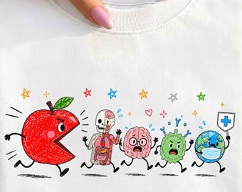 May include: A white crewneck sweatshirt featuring a colorful graphic of a large red apple chasing a human anatomy figure, a brain, a green cell, and a globe wearing a face mask. The design includes small multi-colored stars and a medical cross sign.