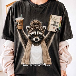 Cute Homeschool Mom Printable PNG Design featuring a stylish raccoon wearing reading glasses, a leopard-print headband with a messy bun, and a cozy cardigan. The raccoon proudly holds an iced coffee labeled "Fueled by Coffee" in one hand and a lesson planner in the other, with the words "Homeschool Mom" below. Perfect for homeschool moms, home educators, coffee lovers, classical education families, Charlotte Mason enthusiasts, sublimation crafts, POD projects, and thoughtful homeschool gifts.