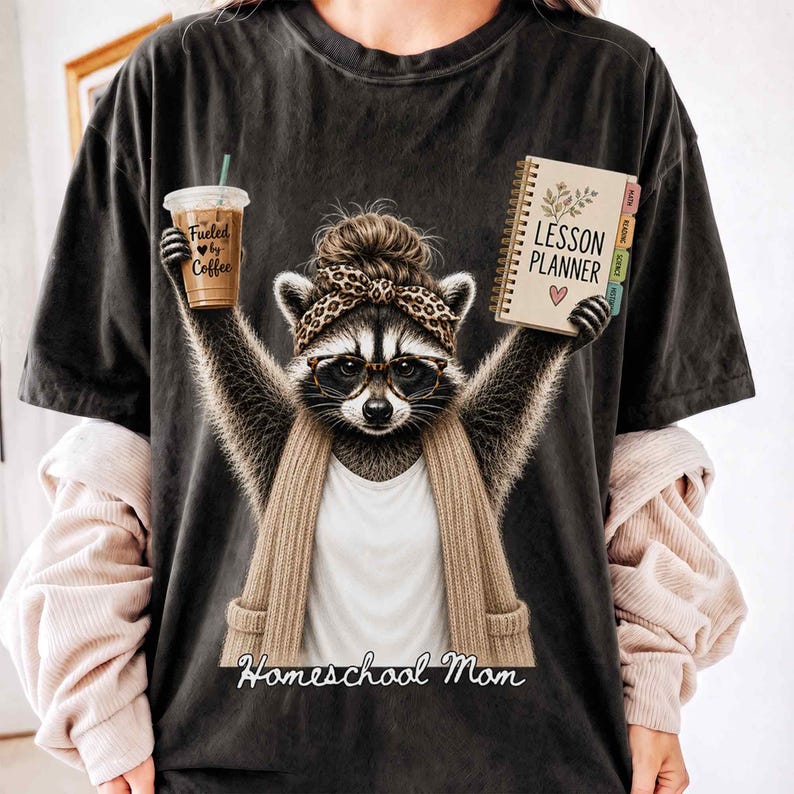 Cute Homeschool Mom Printable PNG Design featuring a stylish raccoon wearing reading glasses, a leopard-print headband with a messy bun, and a cozy cardigan. The raccoon proudly holds an iced coffee labeled "Fueled by Coffee" in one hand and a lesson planner in the other, with the words "Homeschool Mom" below. Perfect for homeschool moms, home educators, coffee lovers, classical education families, Charlotte Mason enthusiasts, sublimation crafts, POD projects, and thoughtful homeschool gifts.