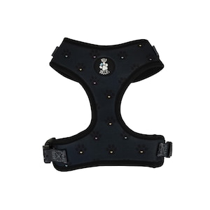 Op de afbeelding: Zwart hondentuig met een pootafdrukpatroon en de tekst "Wild Doggies". Het tuig heeft verstelbare bandjes en een gespsluiting. De pootafdrukken zijn in zwart, roze en goud.