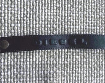 Bracciale Diesel in pelle nera con logo DIESEL in rilievo, chiusura regolabile con bottone a pressione, cinturino unisex di design.