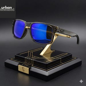 May include: Sunglasses with blue lenses and a black frame, presented on a black and gold stand. The stand has a geometric design. The sunglasses are labelled "POLARIZED". The text "urban streetthood" is visible in the top left corner.