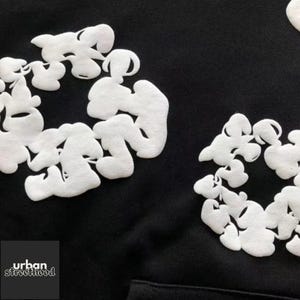 May include: Black hoodie with white, cloud-like, abstract design elements. The design is repeated across the fabric. The lower left corner features the text "urban streetthood" in white.