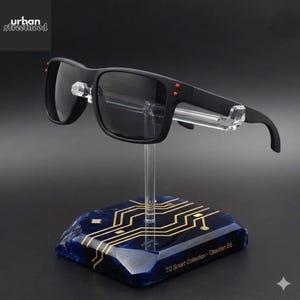 Puede incluir: Gafas de sol negras con montura rectangular y lentes oscuras, expuestas sobre un soporte transparente. El soporte est&aacute; montado sobre una base azul con un dise&ntilde;o de placa de circuito dorado. El texto "TG Smart Collection - Obsidian Ed." es visible.