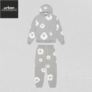 May include: A gray hoodie and matching sweatpants set. The clothing set features a white floral pattern. The hoodie has a drawstring hood and a front pocket. The sweatpants have a drawstring waist. The Urban Street Hood logo is in the top left corner.
