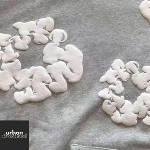 May include: Close-up of a gray sweatshirt with white, cloud-like appliqu&eacute;s. The design is repeated across the fabric. The lower left corner features the text "urban streetthood" in a white, sans-serif font.