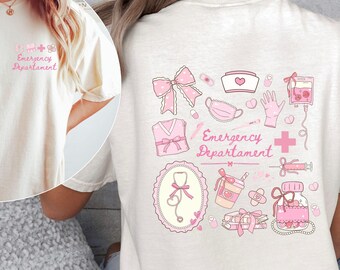 Puede incluir: Camiseta color crema con gráficos rosas de temática médica. La parte delantera presenta un pequeño diseño con una cruz y texto. La parte trasera muestra un diseño más grande con ilustraciones de elementos médicos, incluyendo un lazo y el texto "Emergency Department".